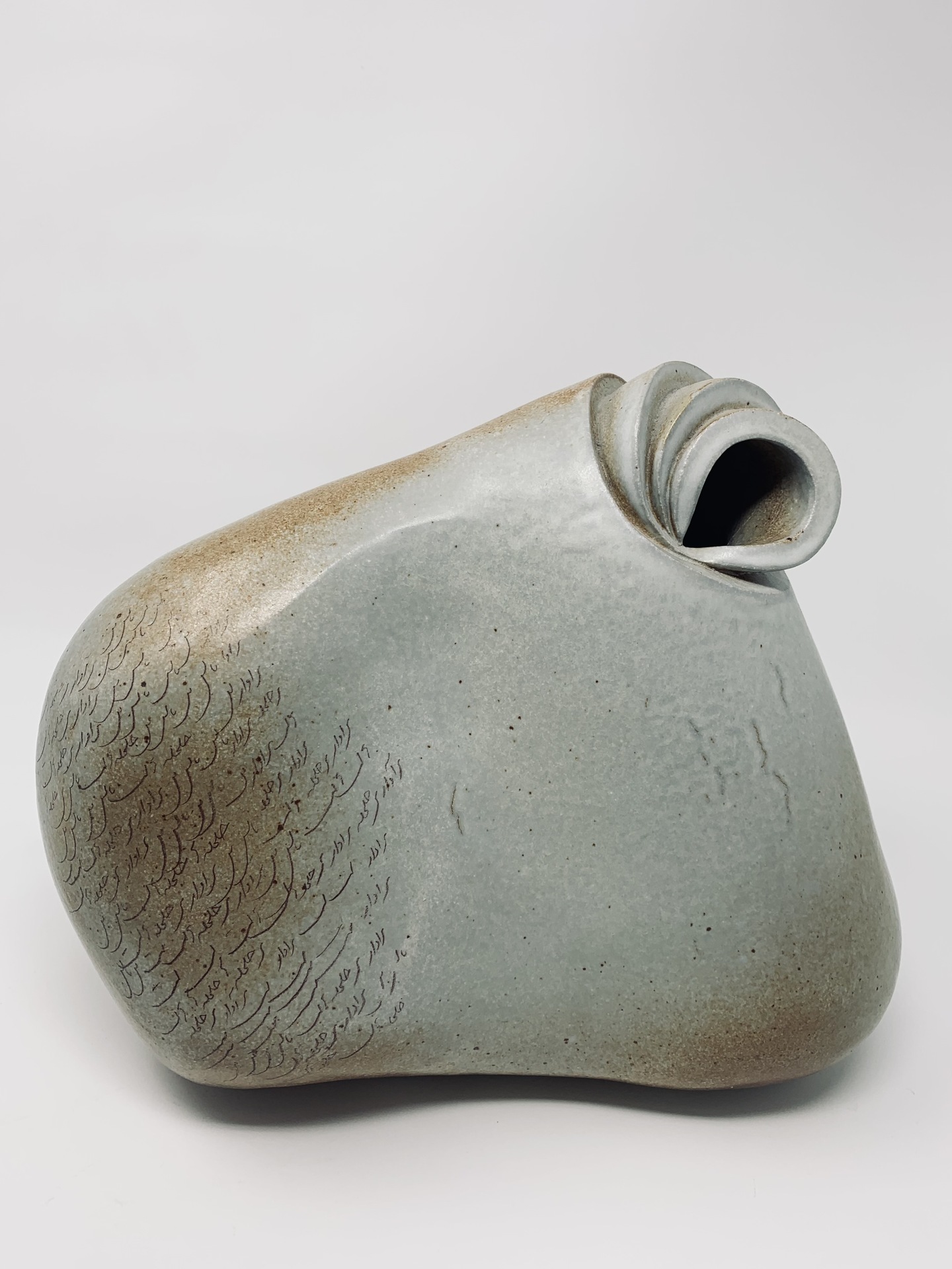 Shahin Massoudi clay vast with small twirl opening on the left side is inscribed with a poem from the artists' Iranian culture.